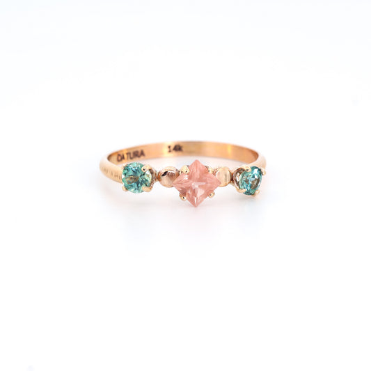 Gold ring with a star-shaped pink gemstone and two smaller green gemstones on a white background
